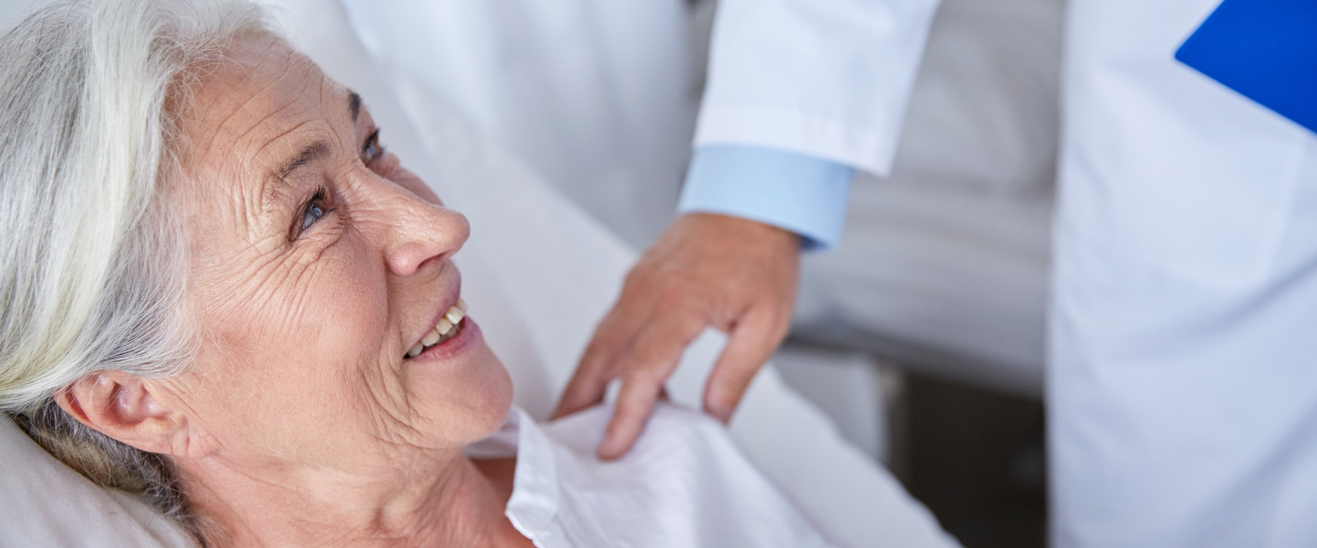 Ältere Patientin im Bett schaut zu Arzt auf